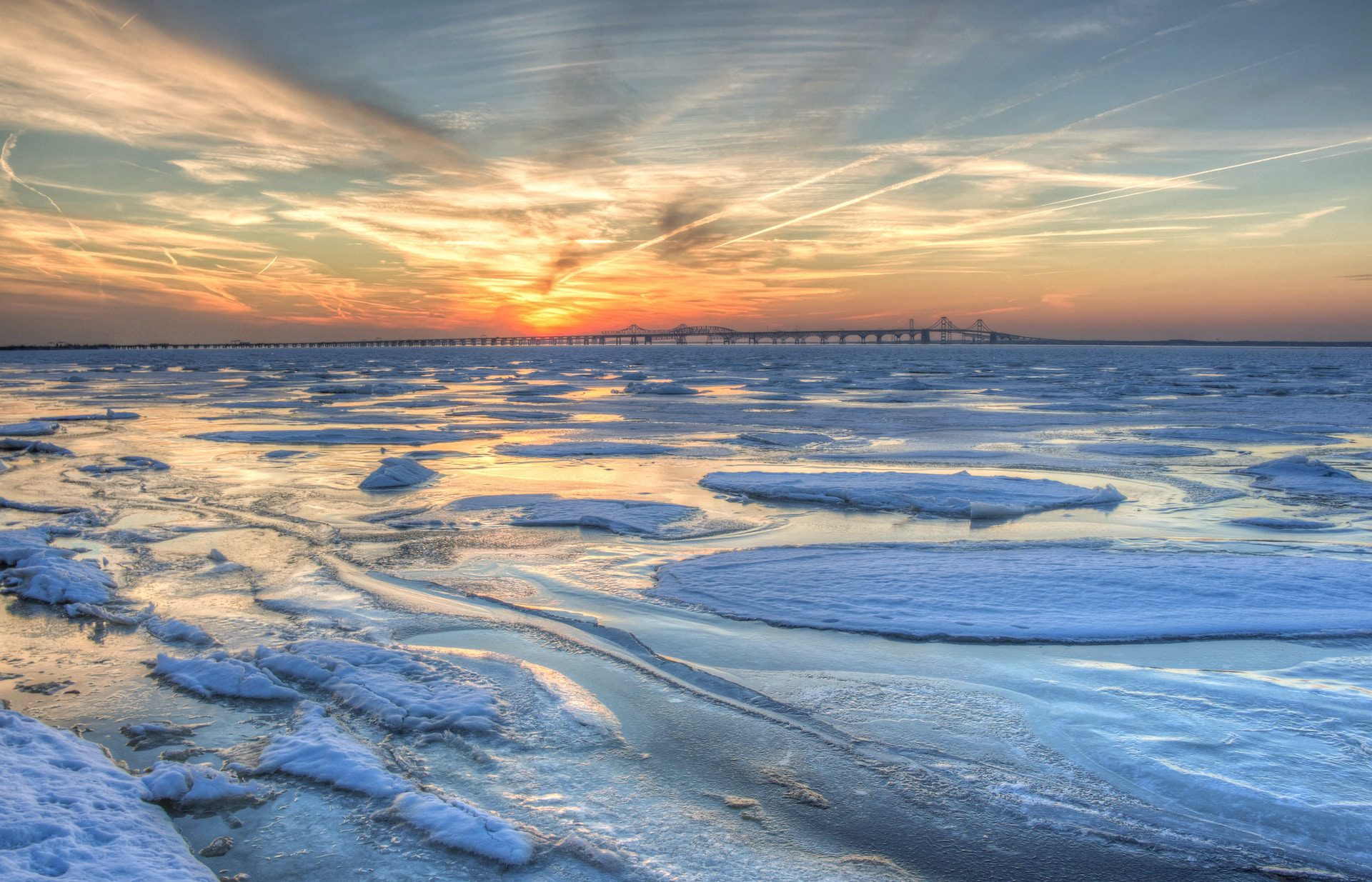 body of water with patches of ice and a bridge in the background