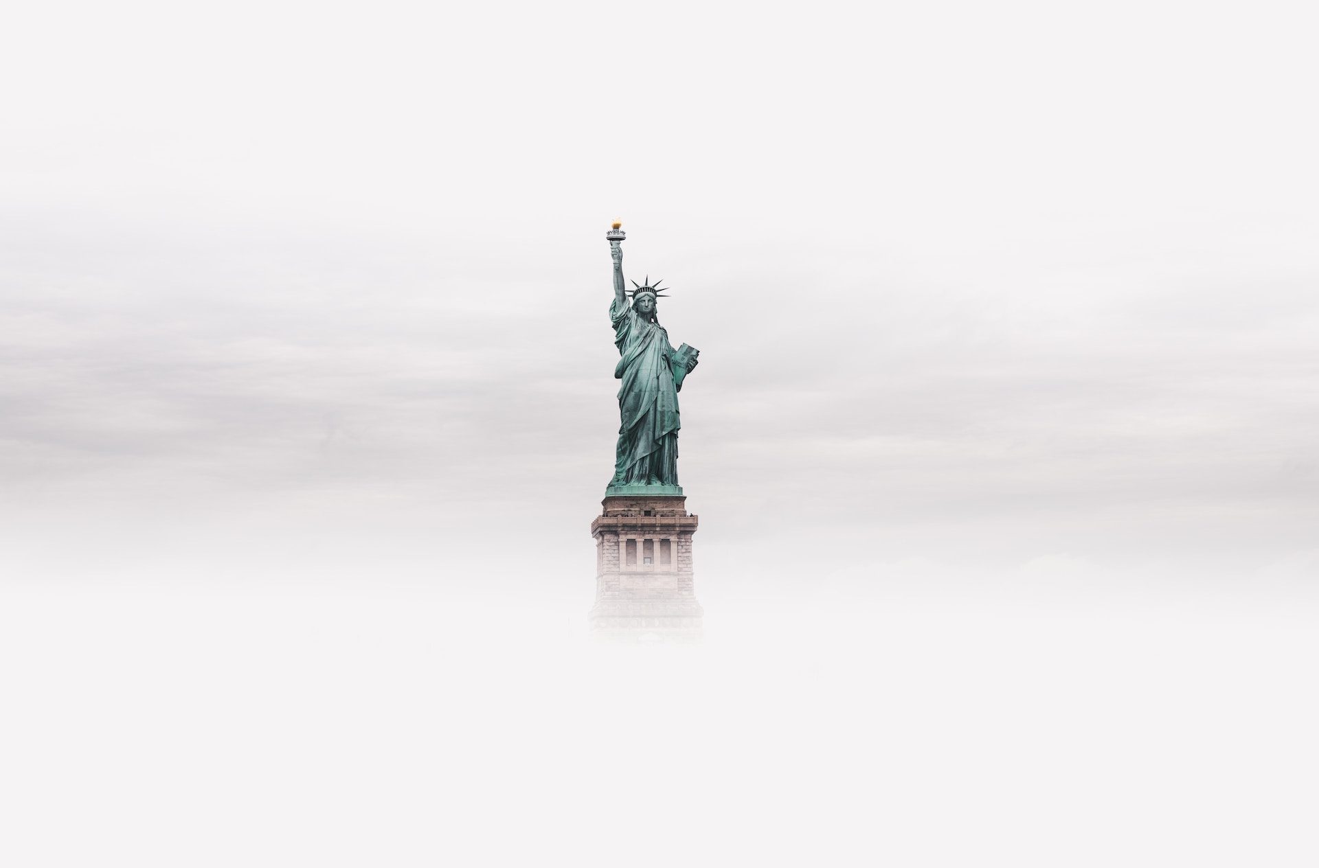 statue of liberty peeking through mist and clouds in the background