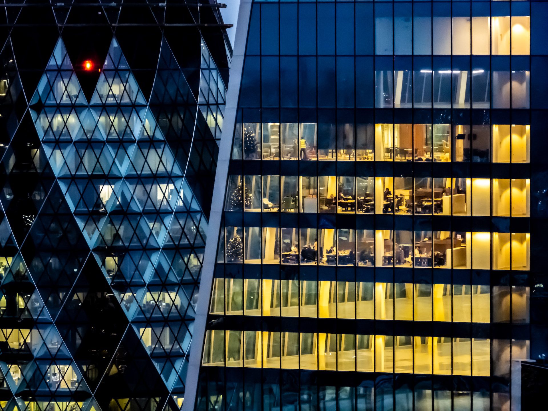 close up shot of buildings and offices lit up in the evening with desks and people in the windows of the buildings