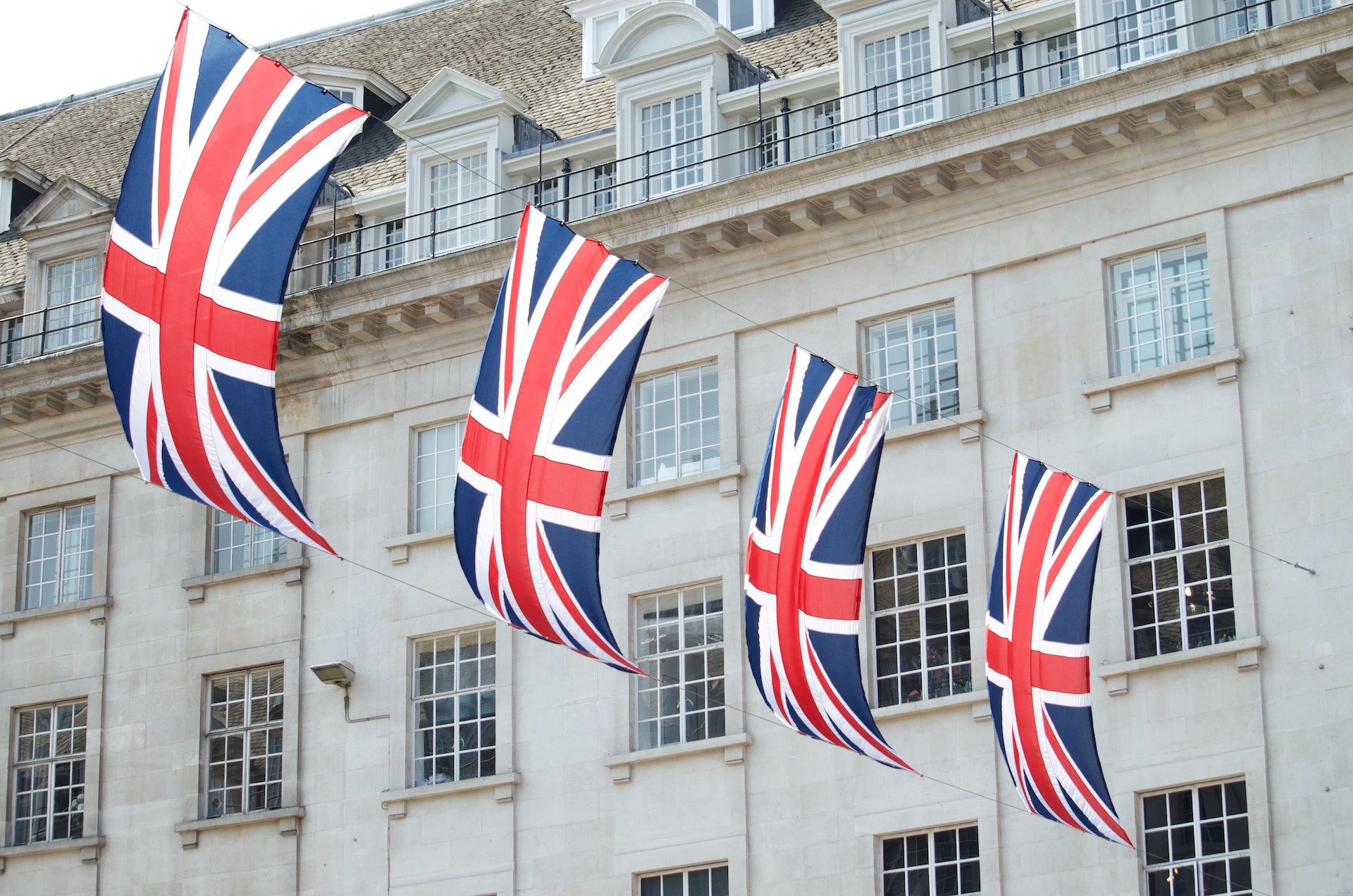 row of four flags of England in front of white building