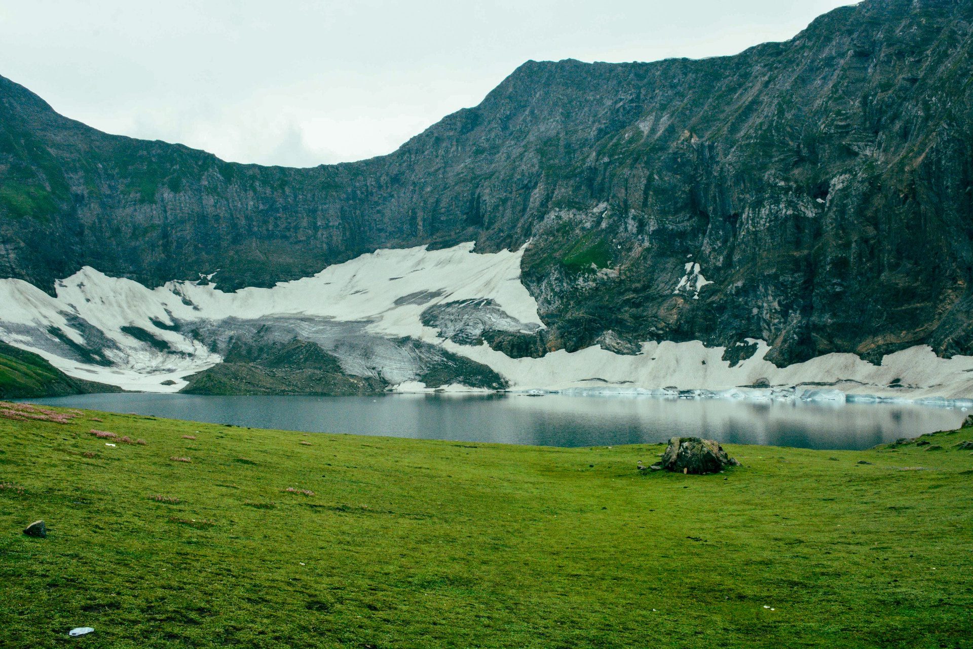 green grass in foreground with a lake and mountains with snow in the background