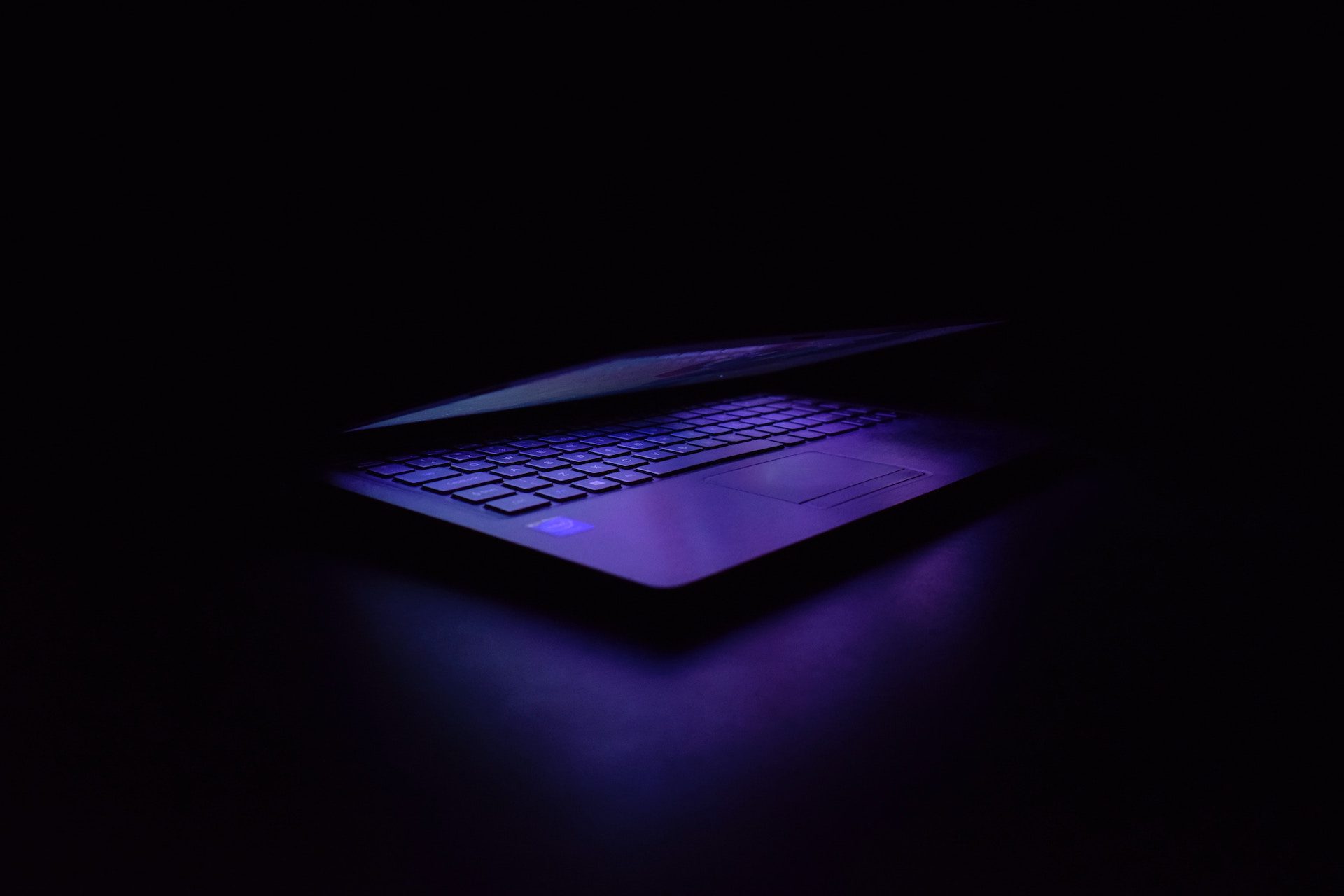 laptop half closed with purple light shining against a dark black background