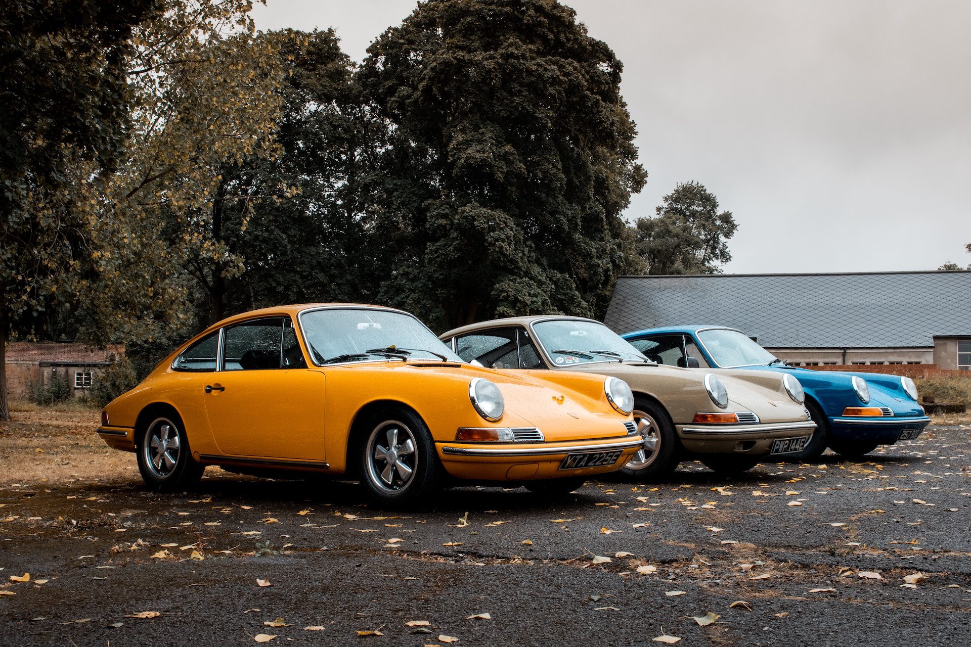 row of 3 Porsche 912 cars parked with trees and a building in the background